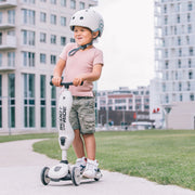 Child riding a scooter with a helmet on a sidewalk in an urban setting