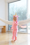 Child in a pink unicorn costume standing in a room with a hammock.