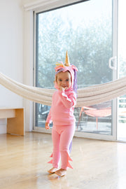 Child in a pink unicorn costume standing in a room with a hammock.