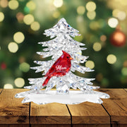 Crystal Christmas tree with a red cardinal figurine on a wooden surface, blurred festive lights in the background.