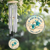 Wind chime with turtle design and personalized text hanging among green leaves.